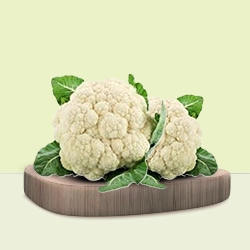 Crisp white cauliflower heads arranged with green leaves on a rustic wooden board.